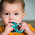 A baby chews a teething toy, a generally safe way to alleviate teething pain.