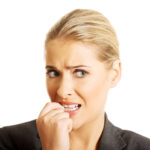A young blond woman chews her nails out of stress, a habit our Placerville dentists discourage.