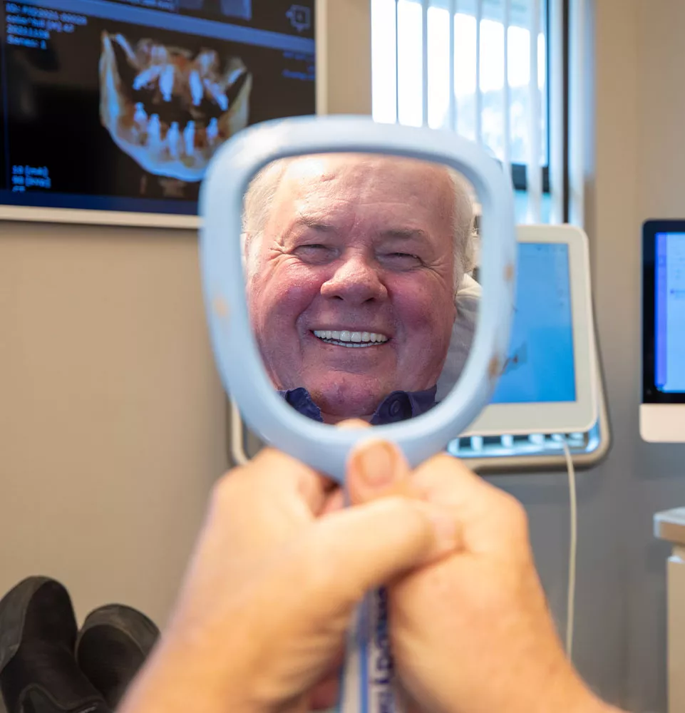 Man smiling into a mirror during his dental visit