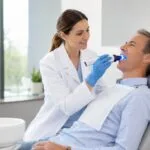 Dentist performing a VELscope oral cancer screening on a relaxed patient using a handheld blue-light device.